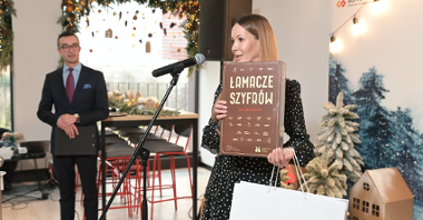 Zdjęcie przedstawia dyrektor Biura Obsługi Inwestorów Katję Lożinę. Prezentuje grę planszową "Łamacze szyfrów".