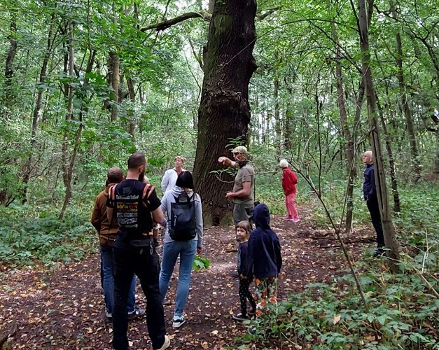 Grupa spacerowiczów po użytku ekologicznym stoi na tle dużego drzewa i słucha opowiadań przewodnika - grafika artykułu